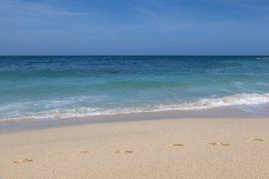 Cornwall 'da kumlu bir sahil, kumların üzerinde ayak izleri ve mavi bir gökyüzü.