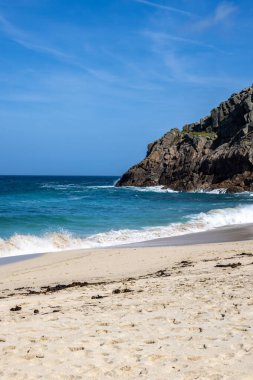 Cornish sahilindeki Portheras Koyu 'nda okyanus manzaralı, üzerinde mavi bir gökyüzü var.