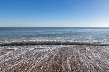 Sussex, Eastbourne 'daki çakıl taşlı sahilde dalgalar, tepemizde mavi bir gökyüzü
