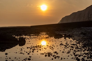 Batan güneş ve sudaki yansıması alçak gelgitte, Sussex 'teki barış cennetinde