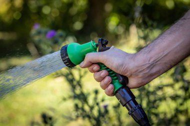 Sığ bir alan derinliği olan bir su akıntısı püskürtürken bir hortum tutuluyor.