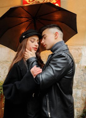 Pizzacının arka planında yağmurda sarılan genç ve güzel bir çift. Şemsiyenin altındaki güzel kız ve erkek. 2 Kasım 2019, Lviv, Ukrayna.