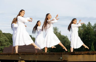 Gentle dance number performed by five girls in white dresses against the background of the lake