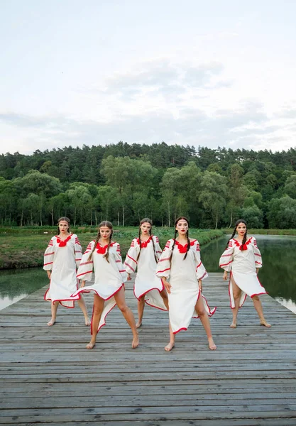 stock image Young people in Slavic clothes  dancing on the pier near the lake. Kupala summer.