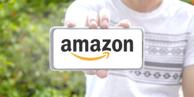 Amazon logosu yazıldı ve akıllı telefondan tek elle tutulup bulanık bir arka plan oluşturuldu.