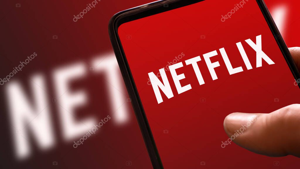 Netflix red logo on mobile phone display with ramp color in the background. streaming movies and TV series platform icon on smartphone screen holding hand. Italy, Milan, 24-01-22