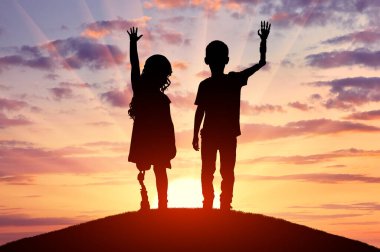 Protez bacakları ve kolları olan iki özürlü çocuğun siluetleri bir tepenin üzerinde duruyor ve batan güneşin arka planına ellerini sallıyorlar. Protez kullanan engelli çocuklar için ilham verici ve motive edici içerik kavramı