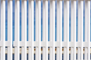 Mavi gökyüzüne ve denize karşı beyaz bir çitin parmaklıkları soyut bir arkaplan olarak