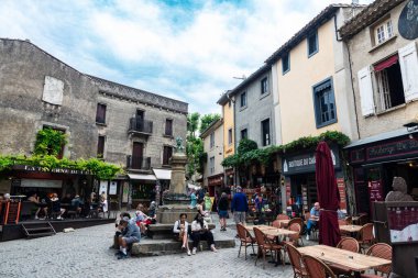 Carcassonne, Fransa - 18 Haziran 2024: Jean-Pierre Cros-Mayrevieille 'in bir alışveriş caddesindeki heykeli Cite de Carcassonne, Occitanie, Fransa' nın duvarlı ortaçağ kalesinin çevresindeki insanlarla birlikte