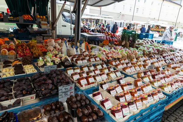 Salzburg, Avusturya - 2 Nisan 2025: Grunmarkt 'ta reçel ve fındıklı meyve ve sebze dükkanı, Salzburg, Avusturya' daki Universitatsplatz 'da insanların bulunduğu sokak yemekleri pazarı