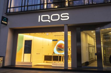 Munich, Germany - April 3, 2025: Sign of the Iqos shop with a line of heated tobacco products of Philip Morris International or PMI in Kaufingerstrabe, shopping street in Munich, Bavaria, Germany 