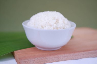 Beyaz kasedeki pirinç ahşap masada ve yeşil duvar arka planında