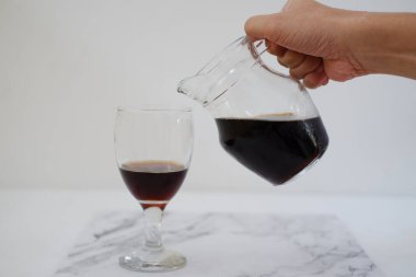 Sürahiden beyaz arka planda bir bardağa kola dökülüyor.