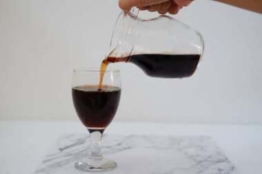 Sürahiden beyaz arka planda bir bardağa kola dökülüyor.