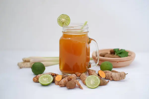 Fresh ginger and lemon juice in a glass jar with ginger roots on white background.