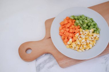 Donmuş sebzeler beyaz bir tabakta beyaz bir mermer masada..