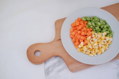 Donmuş sebzeler beyaz bir tabakta beyaz bir mermer masada..