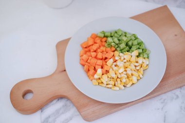 Donmuş sebzeler beyaz bir tabakta beyaz bir mermer masada..