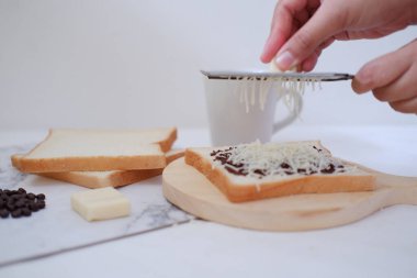 Beyaz arka planda tereyağlı ve çikolatalı tost yapan kadın elleri.