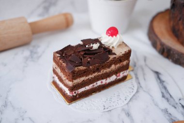 Krem şantili çikolatalı pasta ve beyaz mermer arka planda kirazlar.