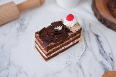 Krem şantili çikolatalı pasta ve beyaz mermer arka planda kirazlar.
