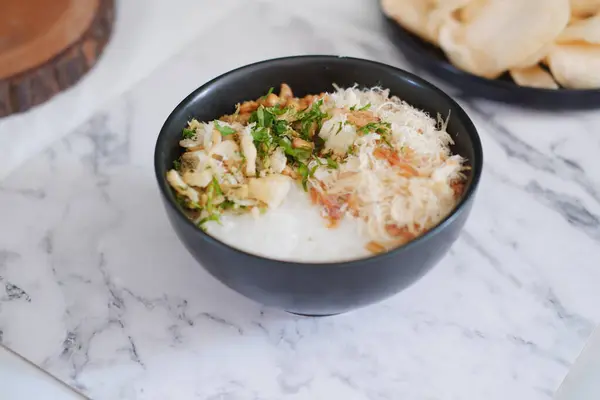 stock image Rice porridge with chicken in black bowl on white marble table