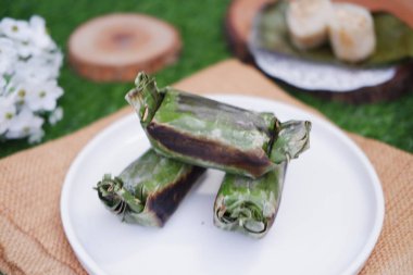 Lemper Bakar. Lemper, glutinous pirinçten yapılmış ve tavuk etiyle doldurulmuş ve muz yapraklarına sarılmış geleneksel bir Endonezya aperatifi. Seçici odak