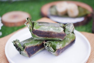 Lemper Bakar. Lemper, glutinous pirinçten yapılmış ve tavuk etiyle doldurulmuş ve muz yapraklarına sarılmış geleneksel bir Endonezya aperatifi. Seçici odak