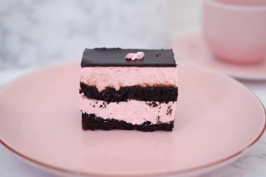 Beyaz mermer masada pembe tabakta bir parça çikolatalı kek..