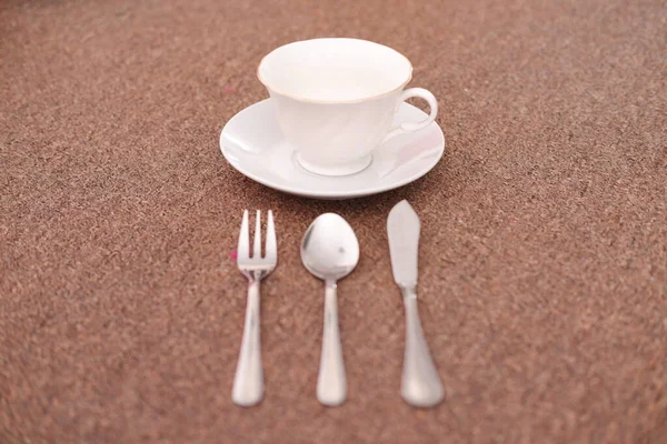 Coffee cup and cutlery on the sand background.