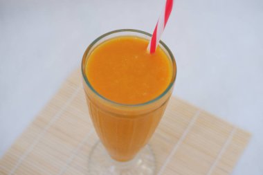 Ahşap masada saman olan bir bardakta mango suyu içeceği..