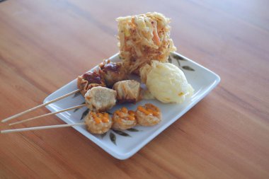 Tahta masadaki beyaz tabakta Tayland usulü kızarmış hamur köftesi.