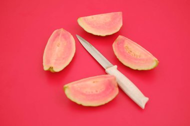 Taze guava meyvesi ikiye bölünmüş ve kırmızı arka planda bıçak var..