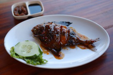 Ahşap masadaki beyaz tabakta baharatlı soslu kızarmış balık..