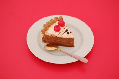 Kırmızı arka planda kaşıkla beyaz tabakta bir parça kek.