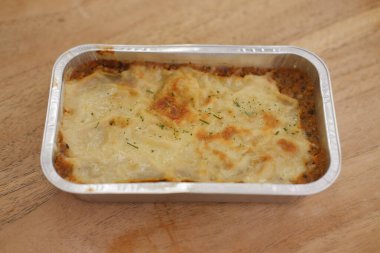 Cannelloni, ahşap bir masada folyo kutusunda peynirle.