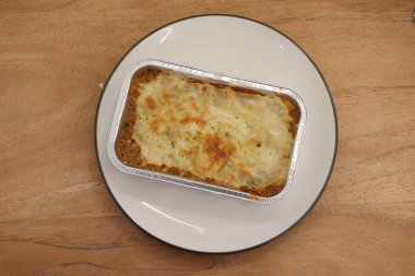 Cannelloni, ahşap bir masada folyo kutusunda peynirle.