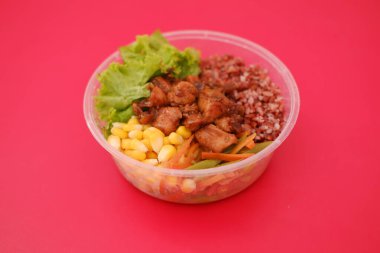 Izgara tavuk, kırmızı pirinç, taze marul, mısır ve karışık sebzelerle dolu plastik bir kase.