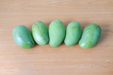 Beş yeşil mango ahşap bir yüzeye dizilmiş.