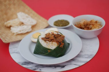 Kırmızı zemin üzerinde et, yumurta, kraker, sambal ve erişte olan pirinç.