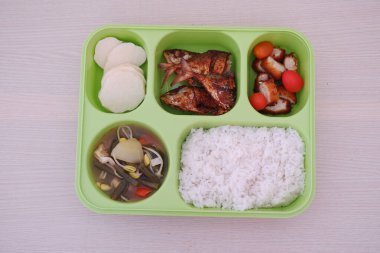 İçinde beyaz pirinç, köri, salatalık ve domates, haşlanmış yumurta, bıldırcın yumurtası, kızarmış tavuk ve bir parça et bulunan yeşil tepsi.