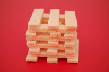 Kremalı bej renkli gofret kurabiyeleri parlak kırmızı bir yüzeye saçılmış.