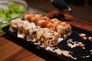 Somon, avokado, peynir ve siyah tabakta soslu suşi.