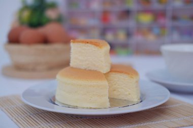 Beyaz tabakta peynirli kek ve bambu hasırında yumurta.