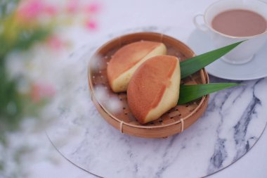 Geleneksel yumuşak ve kabarık bir kekin iki parçası. Altın kahverengi kabuklu. Örgü bambu tepside servis ediliyor.