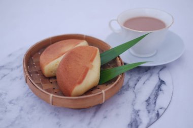 Yuvarlak bir bambu tepsisinin içinde iki tane altın sarısı krep ya da yumuşak sünger keki var. Büyük ihtimalle geleneksel Endonezya atıştırmalıkları. Kue apem ya da kue dorayaki olarak bilinir.