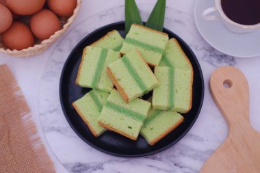 Lezzetli katmanlı pandan keki siyah bir tabakta yumurta ve kahveyle dilimlenmiş.