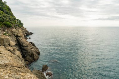 Kıyı kayalığı ve bulutlu gökyüzünün altında sakin bir deniz.