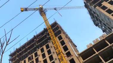 Bottom view of a yellow high-rise construction crane. Construction of a multi-storey brick house. City construction site.