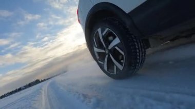 An exciting road adventure. Close-up of the rear right wheel of the SUV. A white car is driving through a snowy field. The littered horizon is like a dynamic reception. Traveling by car in winter.